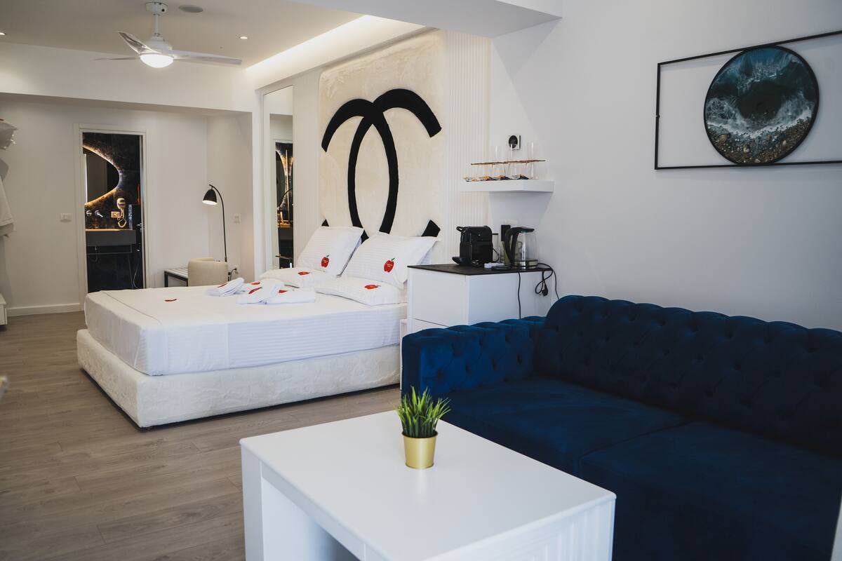 A modern bedroom with a large bed, a blue sofa, a white coffee table, and a wall-mounted artwork.