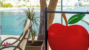 Un balcon donnant sur une ville côtière, une décoration en forme de cœur rouge et une chaise.