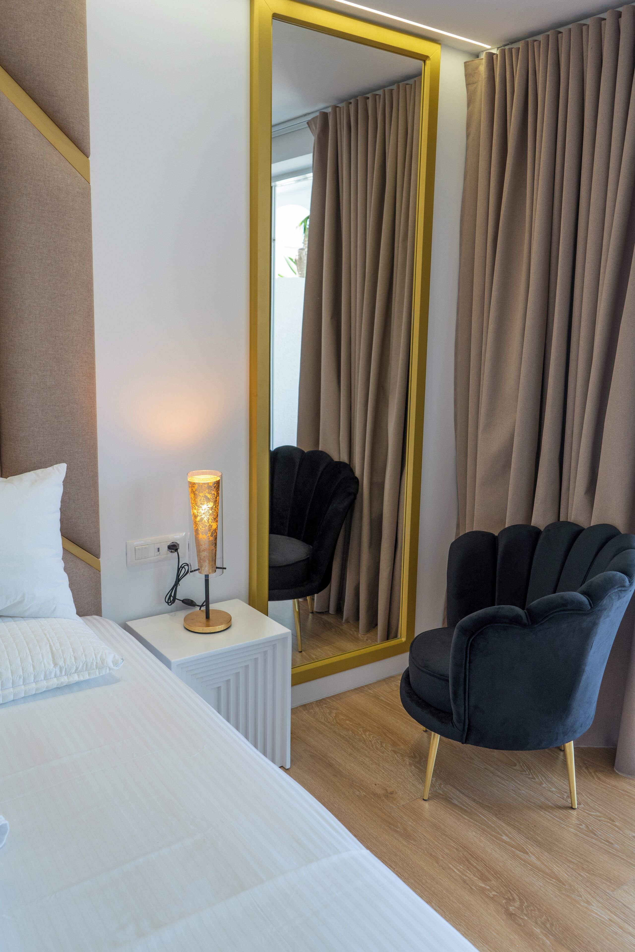 Une chambre d’hôtel avec un lit, une table de chevet avec une lampe, une chaise et un grand miroir.