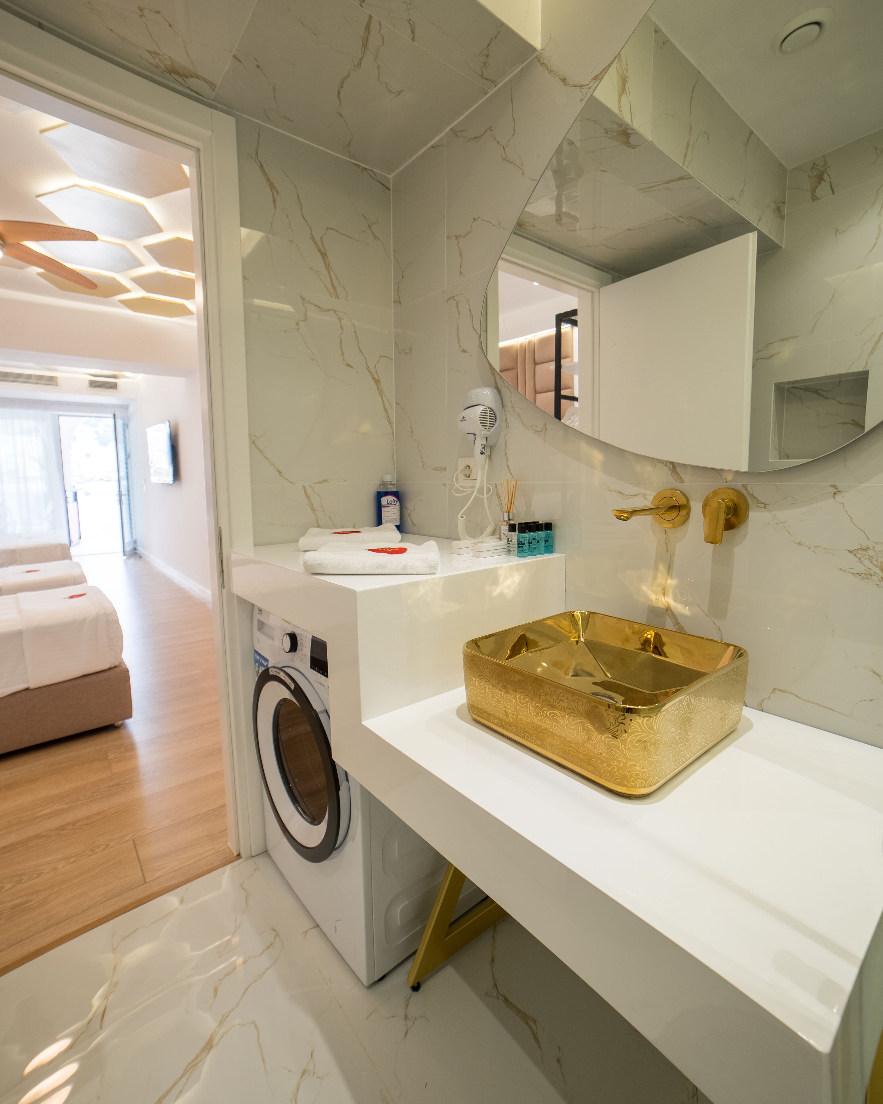 A modern bathroom with a marble backsplash, a gold vanity, a washing machine, and a mirror above the sink.