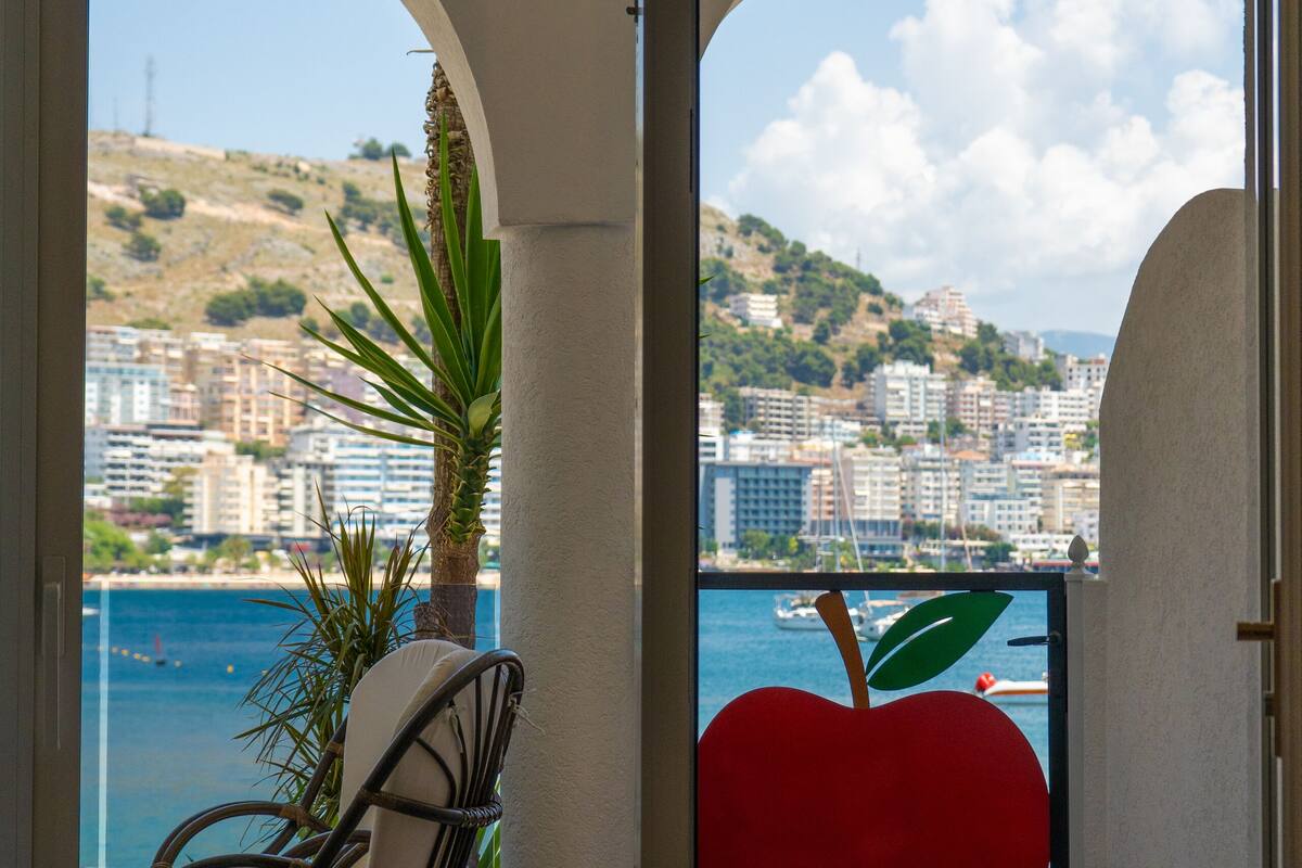 A balcony with a view of a city and sea, a red apple decoration, and a chair.
