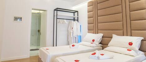 A hotel room with two beds, a ceiling fan, a wardrobe, and a shower area.