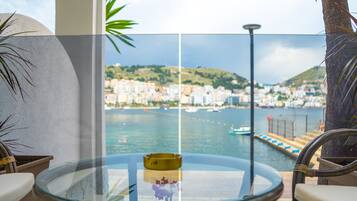 A balcony with a glass table, chairs, and a view of a coastal cityscape with buildings and boats.