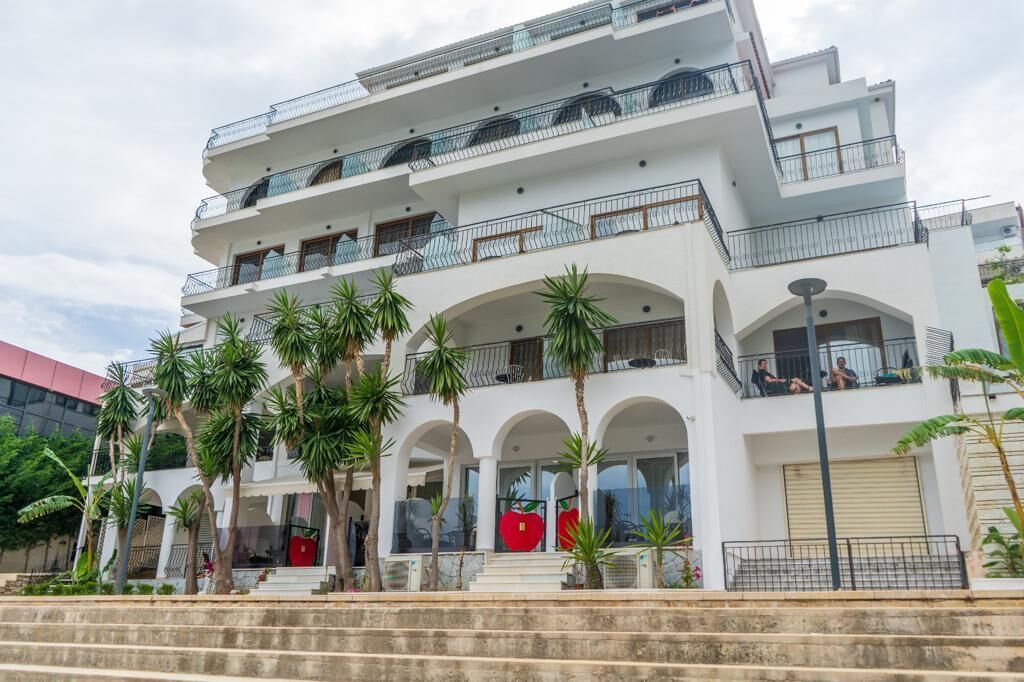 A multi-story hotel with balconies, palm trees, and a red apple decoration.
