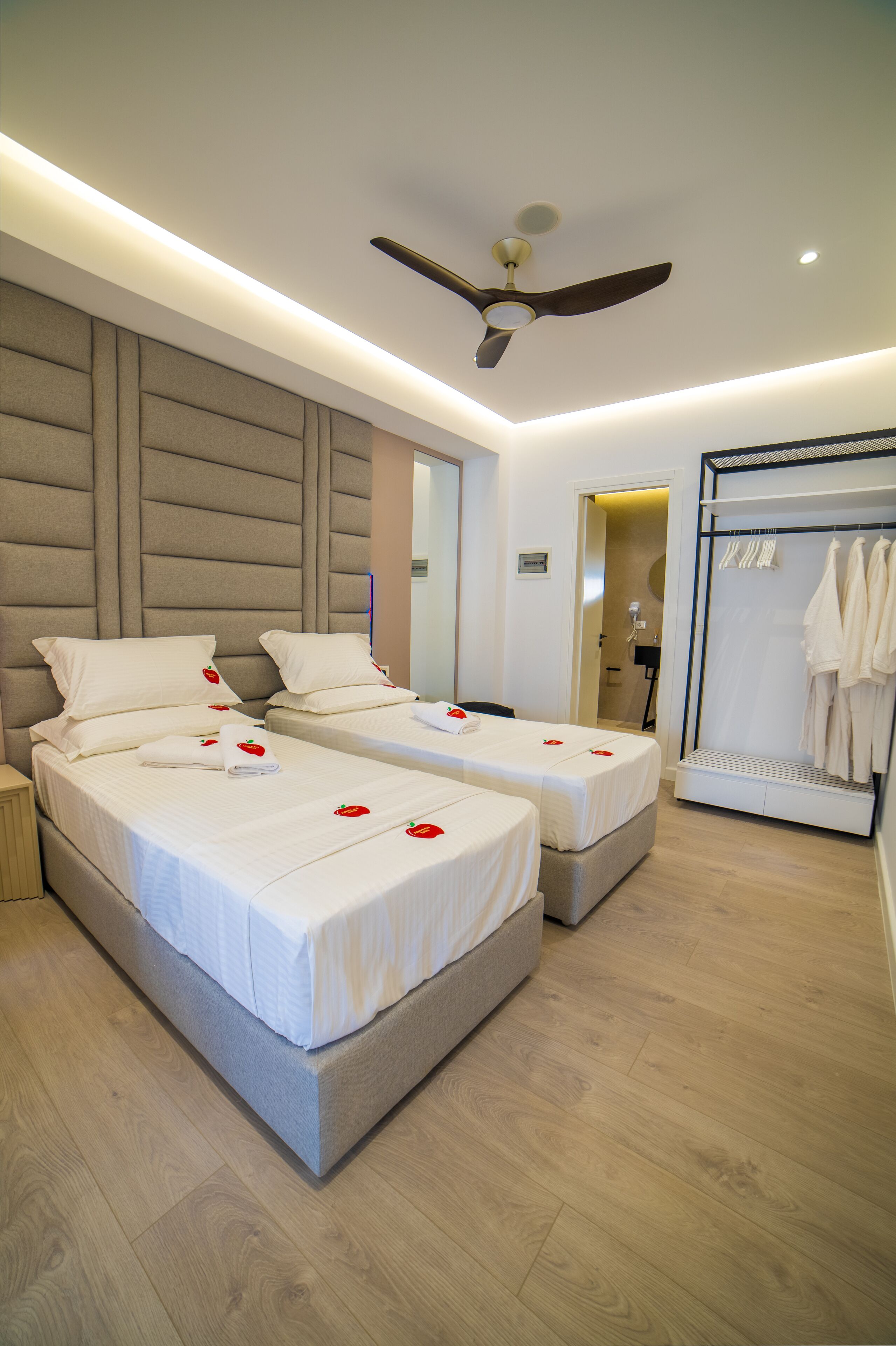 Habitación de hotel con dos camas, ventilador de techo, vestidor y zona de ducha.