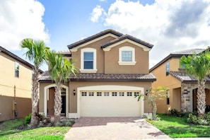 A two-story house with a beige facade, a white garage door, and a brick driveway.