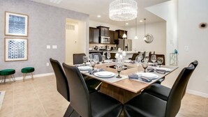 Un coin repas avec une table en bois dressée pour six personnes, des chaises noires et un lustre.