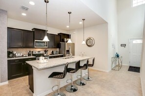 A modern kitchen with dark cabinets, a central island with bar stools, stainless steel appliances, and pendant lighting.