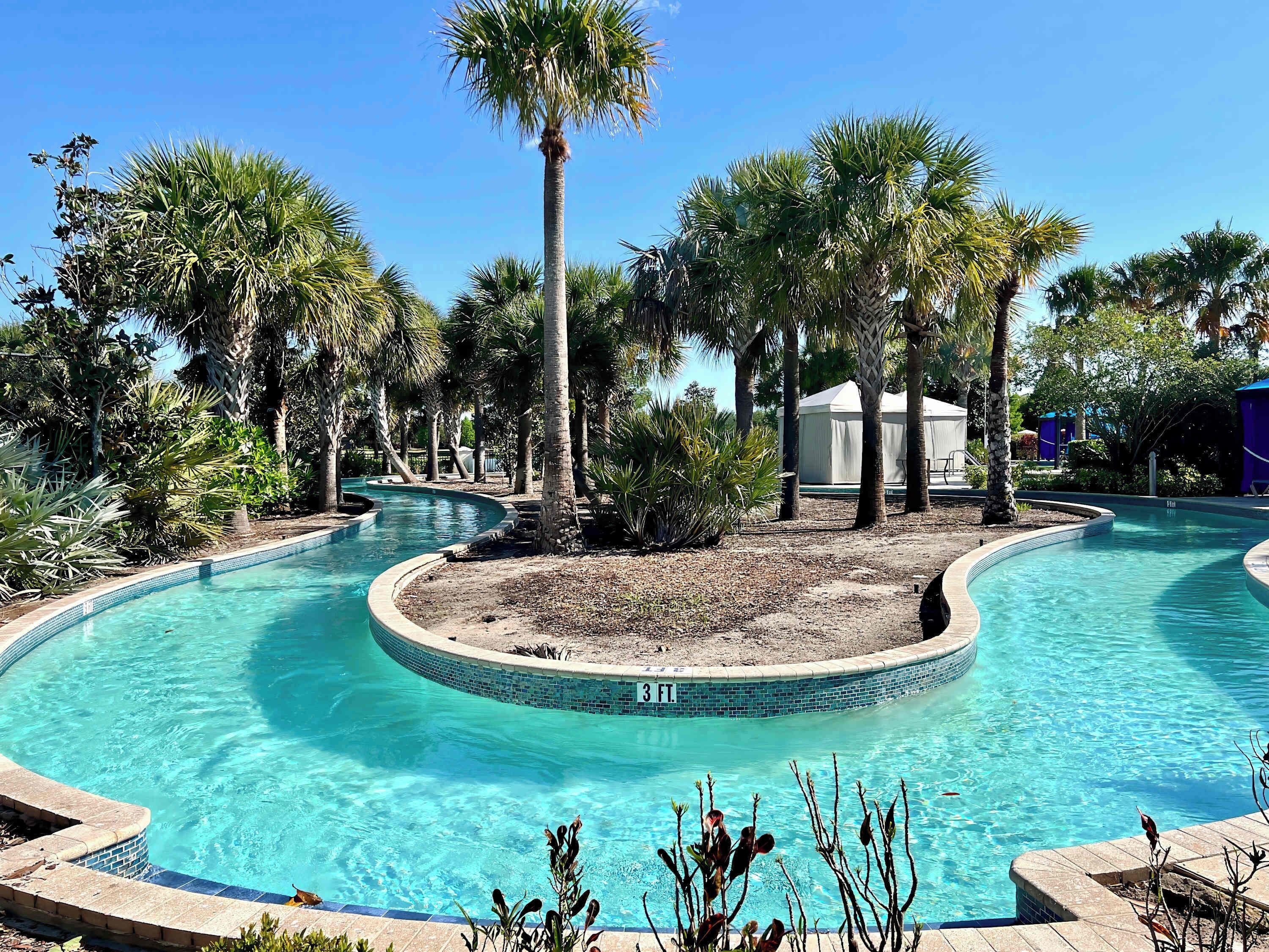 A swimming pool with a 3 ft. depth marker, surrounded by palm trees and a small building in the background.