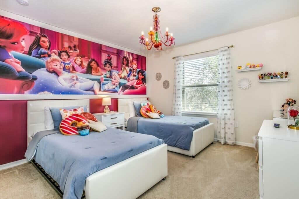 A bedroom with two beds, a large wall mural, a chandelier, and a window with curtains.