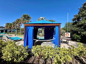 Un mirador con cortinas azules, un área de piscina con sillones de descanso y un letrero que indica zona prohibido fumar.