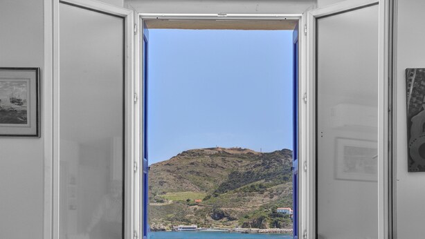 A room with a large window offering a view of a hillside and a body of water.