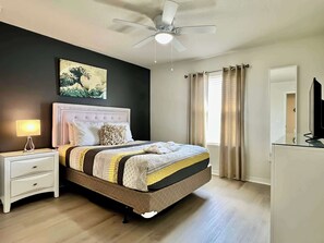 Une chambre à coucher avec un lit, une table de chevet, une lampe, un ventilateur de plafond et un tableau au mur.