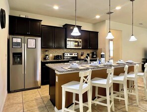 A modern kitchen with dark cabinets, stainless steel appliances, a central island with bar stools, and pendant lighting. - Near Disney | Pool, Spa & Waterslides | Value 2112 (Kissimmee)