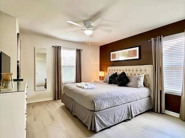 Une chambre à coucher avec un lit, un ventilateur de plafond, une table de chevet avec une lampe et une fenêtre avec des rideaux.