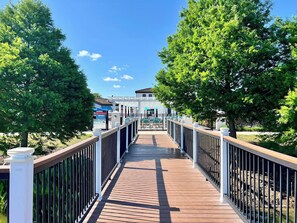A wooden boardwalk leading to a building with a pool area, surrounded by trees.