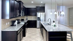 Une cuisine moderne avec des meubles de couleur sombre, des appareils en acier inoxydable, des plans de travail en granit et des luminaires suspendus.
