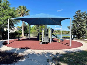 A playground with a red rubberized surface, a blue canopy, and a slide. - Near Disney | Private Pool & Waterpark Resort 2167 (Kissimmee)