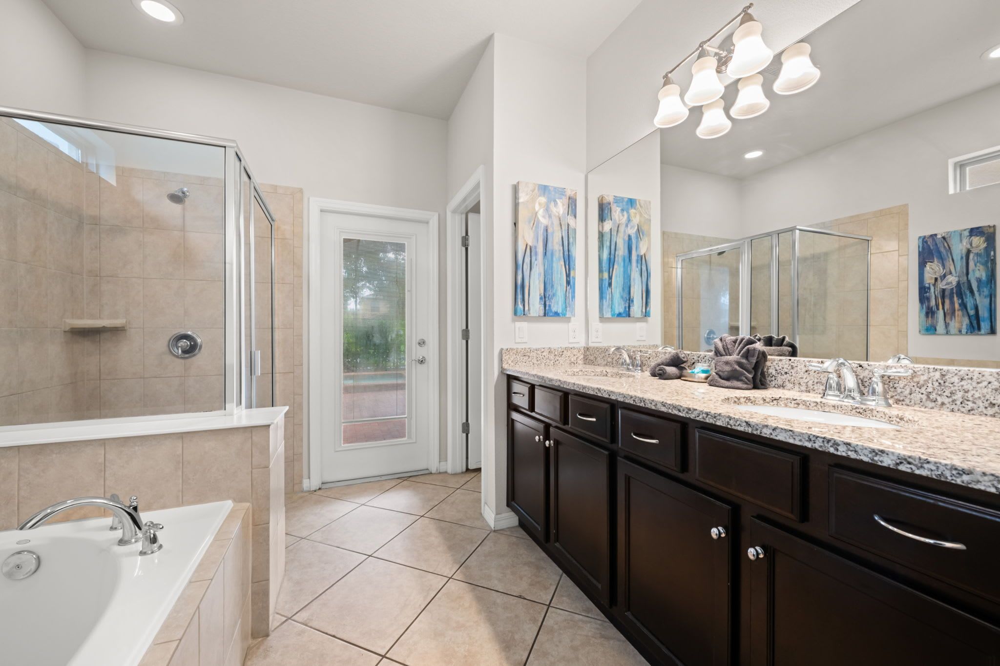 A modern bathroom with a walk-in shower, a large vanity with a granite countertop, and a large mirror.