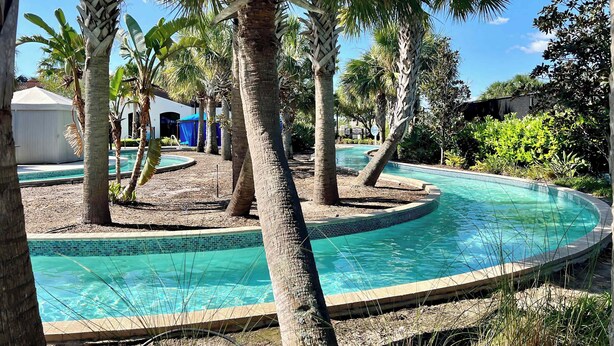 Une piscine entourée de palmiers, un petit bâtiment et un ciel d’un bleu limpide.