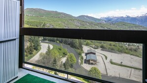 Udsigt fra et vindue over et bjerglandskab med en snoet vej og en bygning med et skraent tag.