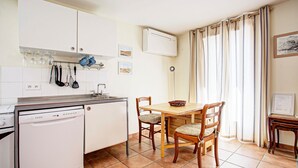 A compact kitchen with a dishwasher, a dining table with chairs, and a window with curtains.