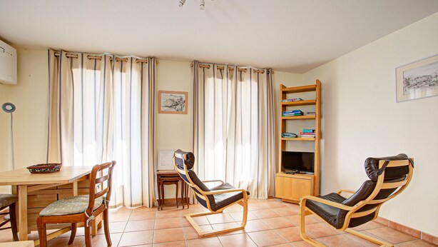 A room with a dining table, two wooden chairs, a sofa, a bookshelf, and a television.