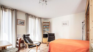 A room with a bed, two chairs, a desk, a bookshelf, and curtains.