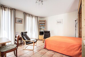 Una habitación con una cama, dos sillas, un escritorio, una estantería y cortinas.