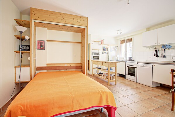 Una habitación compacta con cama, kitchenette y estructura de techo de madera.