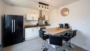 A modern kitchen with a black refrigerator, white cabinets, a wooden countertop, and a coffee station.