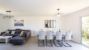 A modern living room with a grey sofa, a dining table with chairs, and a large window.