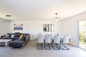 Ein modernes Wohnzimmer mit einer grauen Couch, einem Esstisch mit Stühlen und einem großen Fenster.