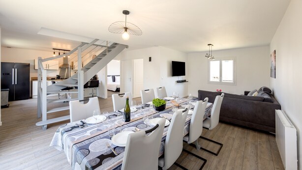 A spacious living area with a dining table set for six, a staircase, and a cozy seating area.