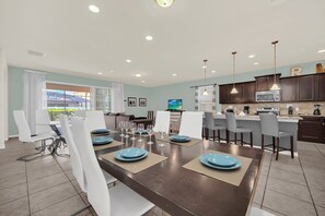 A modern dining area with a dark wooden table set for six, surrounded by white chairs.