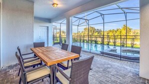 Une terrasse couverte, avec une table en bois et des chaises en osier, donnant sur une piscine et un jardin.