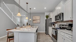 A modern kitchen with white cabinetry, a central island, stainless steel appliances, pendant lighting, and a staircase leading to another level. - Big Screen-Gameroom-Private Pool-6mi 2 Disney-8911 (Four Corners)