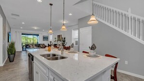 A modern kitchen with a large island, pendant lighting, and a view to the living area. - Big Screen-Gameroom-Private Pool-6mi 2 Disney-8911 (Four Corners)