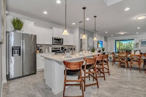Una cocina moderna con armarios blancos, electrodomésticos de acero inoxidable y una isla central con taburetes de bar.
