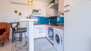 Une cuisine compacte équipée d’un lave-linge, d’un four à micro-ondes et d’un évier. On y trouve un tabouret de bar et une chaise avec un coussin à rayures.
