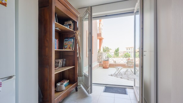 Un couloir avec une bibliothèque en bois, une porte-fenêtre coulissante donnant sur un espace extérieur avec une terrasse et une vue sur un immeuble.