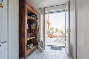 A hallway with a wooden bookshelf, a sliding glass door leading to an outdoor area with a patio and a view of a building. - U Momentu - appt climatisé avec terrasse (L'Île-Rousse)