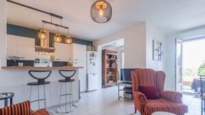 Une cuisine moderne avec des tabourets de bar, un fauteuil à rayures et un téléviseur dans l’espace salon.