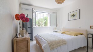 Une chambre à coucher avec un lit, une table de chevet, une fenêtre, un tableau au mur et une porte.