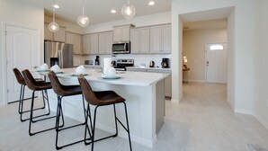 A modern kitchen with white cabinetry, stainless steel appliances, and a central island with bar stools. - Pool! Family Value! Epic Resort 6 mi 2 Disney-8916 (Kissimmee)