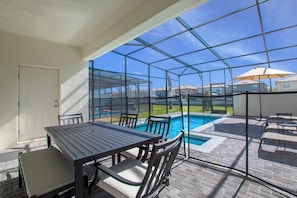 Une terrasse couverte avec une piscine, du mobilier d’extérieur et une vue sur les maisons voisines.