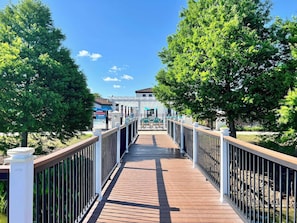 A wooden boardwalk leading to a building with a pool area, surrounded by trees. - Pool Table! Lazy River! Resort 6 mi 2 Disney! 9045 (Kissimmee)