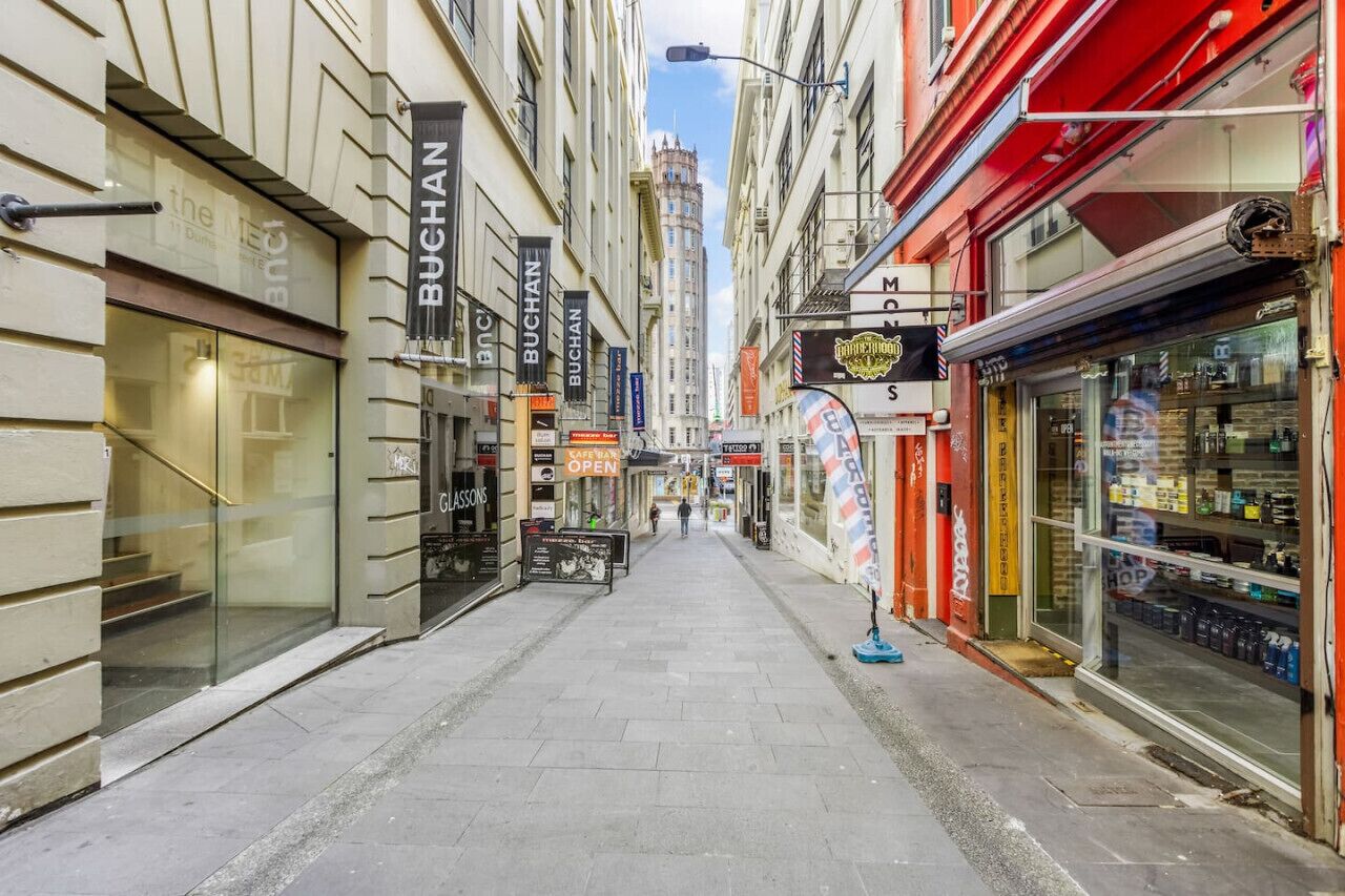 Een smalle stadstraat met diverse winkels en bedrijven, waaronder een gevel met het bord 'BUCHAN'.