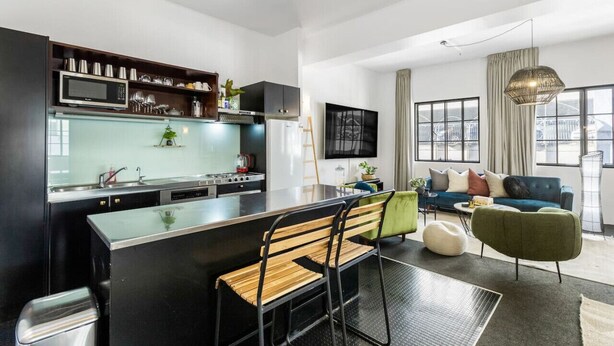 A modern kitchen with a dining area, a living room with a sofa and a TV, and large windows with a view. - Gorgeous NY Style Loft in CBD | Netflix Wifi | (Auckland CBD)