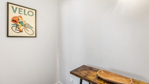 A room with a framed poster of a cyclist on a bicycle, a wooden table with a bowl, and a white wall. - Gorgeous NY Style Loft in CBD | Netflix Wifi | (Auckland CBD)